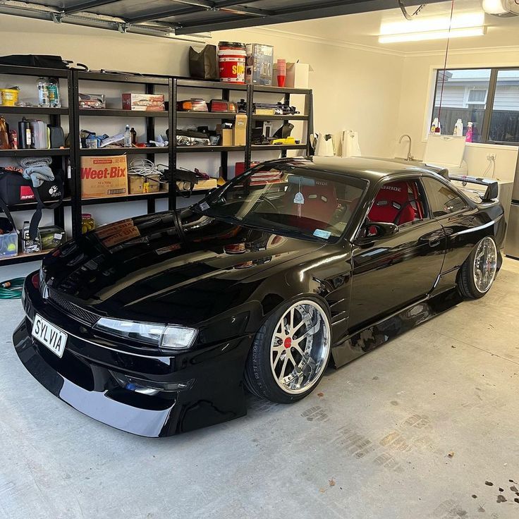 a black car parked in a garage next to shelves filled with tools and other items