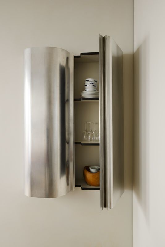 a stainless steel wall mounted cabinet with wine glasses and plates in the bottom shelf, next to a white wall