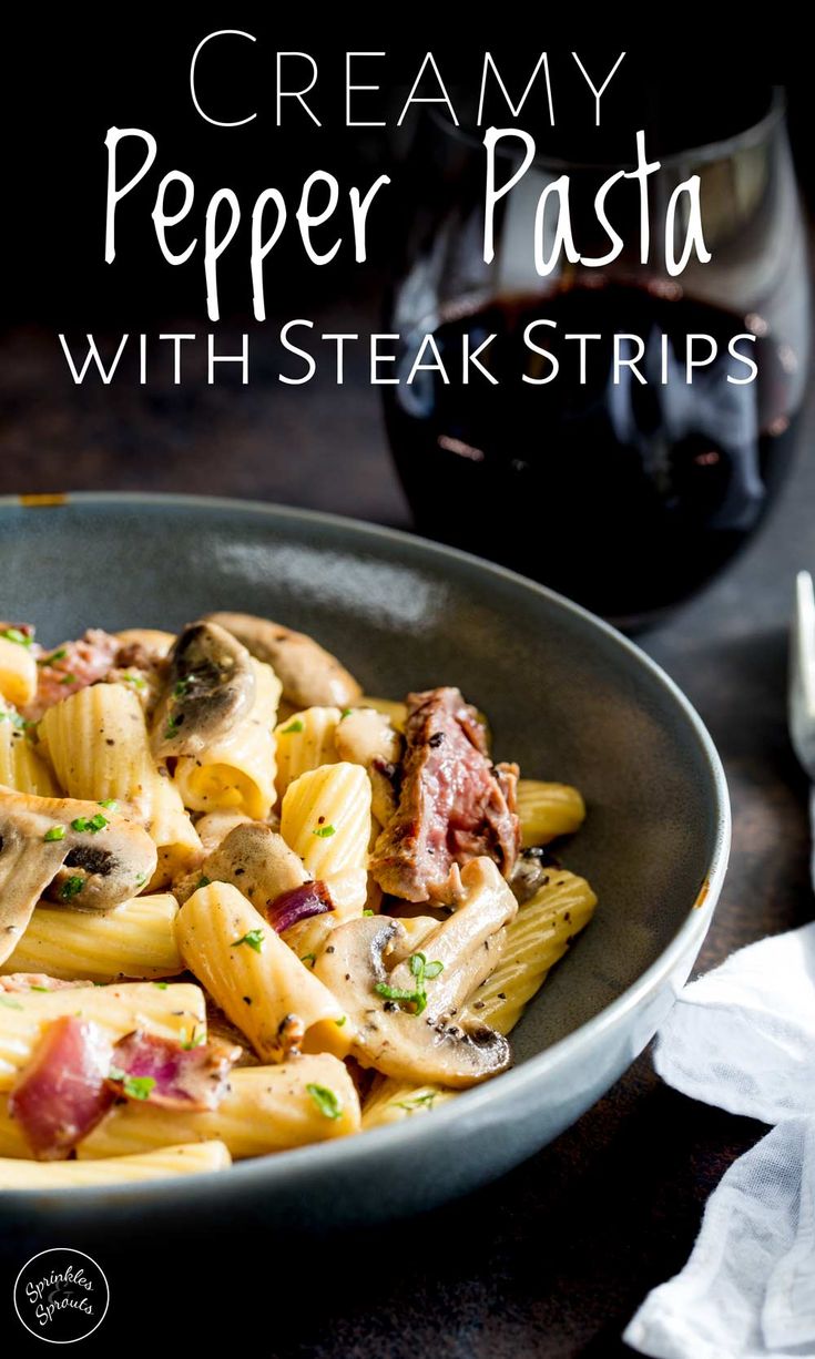 creamy pepper pasta with steak strips in a bowl next to a glass of red wine