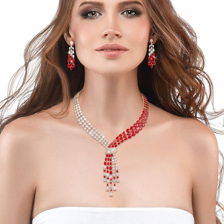 This exquisite set, draped in radiant yellow gold, exudes a timeless charm, while the sparkling Diamondeau®, flawless simulated diamond, adds a touch of sophistication and glamour. At the heart of this ensemble is a necklace that elegantly flows around the neck, reminiscent of a graceful tie, yet imbued with a sense of femininity and grace. The red and white gems create a mesmerizing contrast that captivates the eye and commands attention. Completing the set are the matching earrings. Each earri Elegant Cubic Zirconia Jewelry Sets For Valentine's Day, Elegant Rhinestone Jewelry Sets For Party, Elegant Diamond White Jewelry Sets For Parties, Elegant Jewelry Sets For Valentine's Day Formal, Diamond White Sparkling Stones Jewelry For Evening, Evening Jewelry With Sparkling Stones In Diamond White, Elegant Diamond White Crystal Jewelry Sets, Diamond White Jewelry With Sparkling Stones For Evening, Diamond White Bridal Necklace For Party