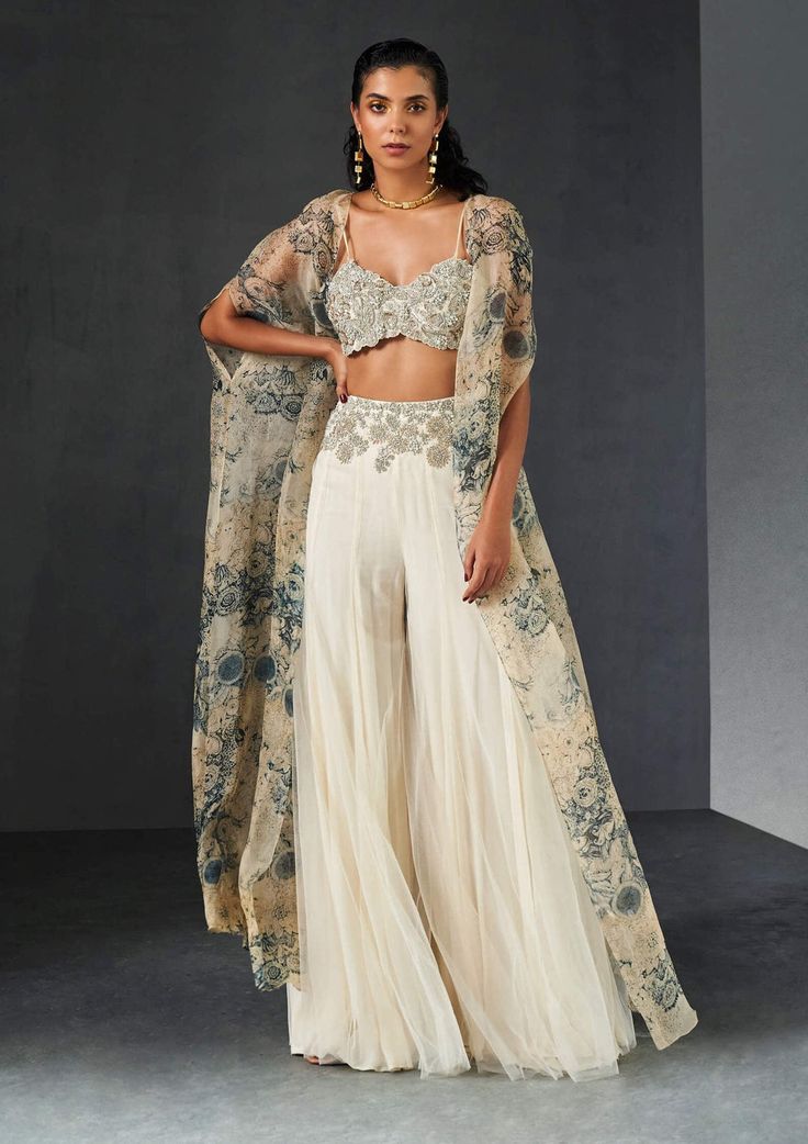 Editor's Note Presenting an exquisite ensemble: a champagne-blue cape that gracefully complements an ambi jaal embroidered bustier and an embroidered waist net sharara. This ensemble effortless... Sharara And Cape, Sangeet Outfit Sharara, Roce Ceremony Outfits, Indian Cape Outfits, Elegant Palazzo Set For Reception With Sheer Dupatta, Elegant Palazzo Set With Sheer Dupatta For Reception, Sheer Dupatta Sets For Eid Reception, Anarkali Set With Sheer Dupatta And Cape Sleeves, Elegant Sets With Cape Sleeves For Eid