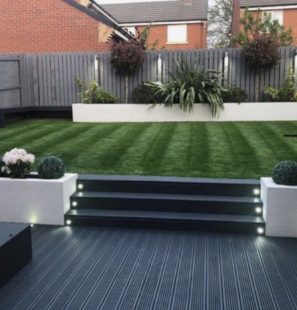 an outdoor area with grass, plants and steps leading up to the back yard is lit by led lights