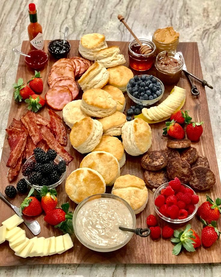 a wooden cutting board topped with different types of food and desserts next to fruit