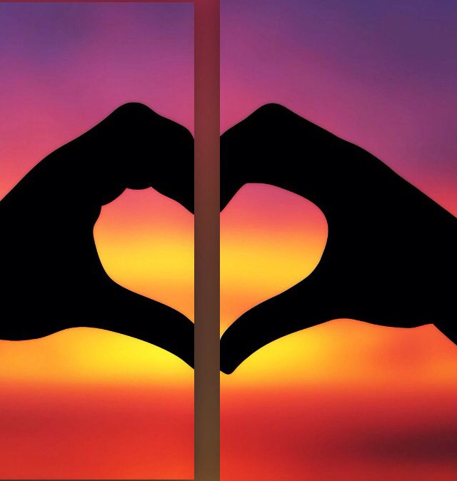 two hands making a heart shape in front of an orange and purple sky at sunset