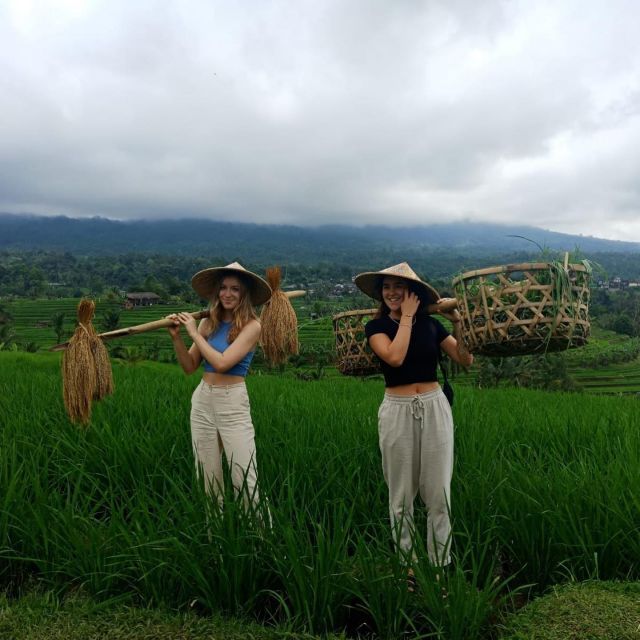 two women are standing in the middle of a field, one holding a broom and the other wearing a straw hat