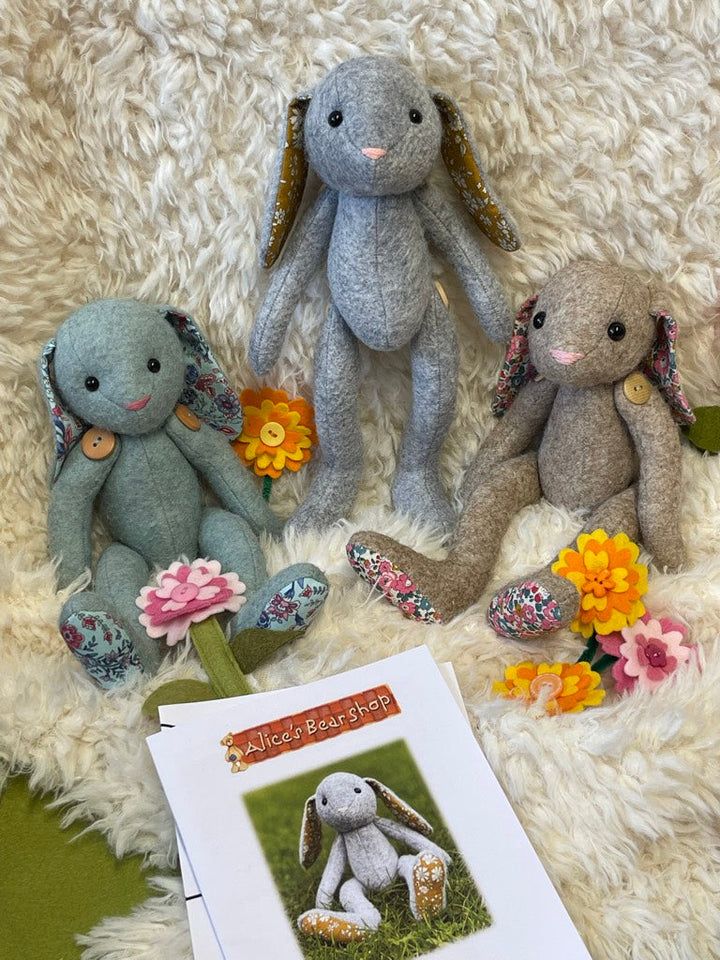 three stuffed animals sitting next to each other on a white rug with flowers and an open book