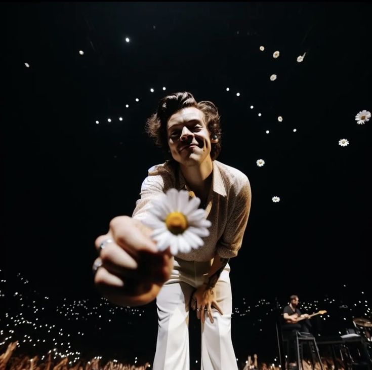 a man holding a flower in his hand while standing next to a stage full of people