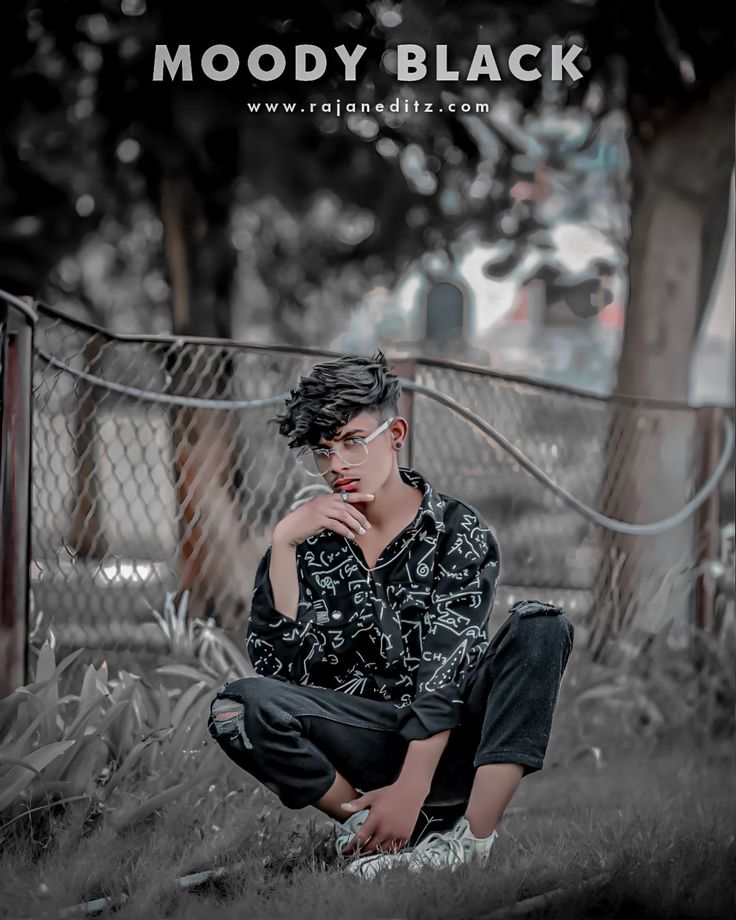 a young man sitting on the ground in front of a fence with his hand under his chin