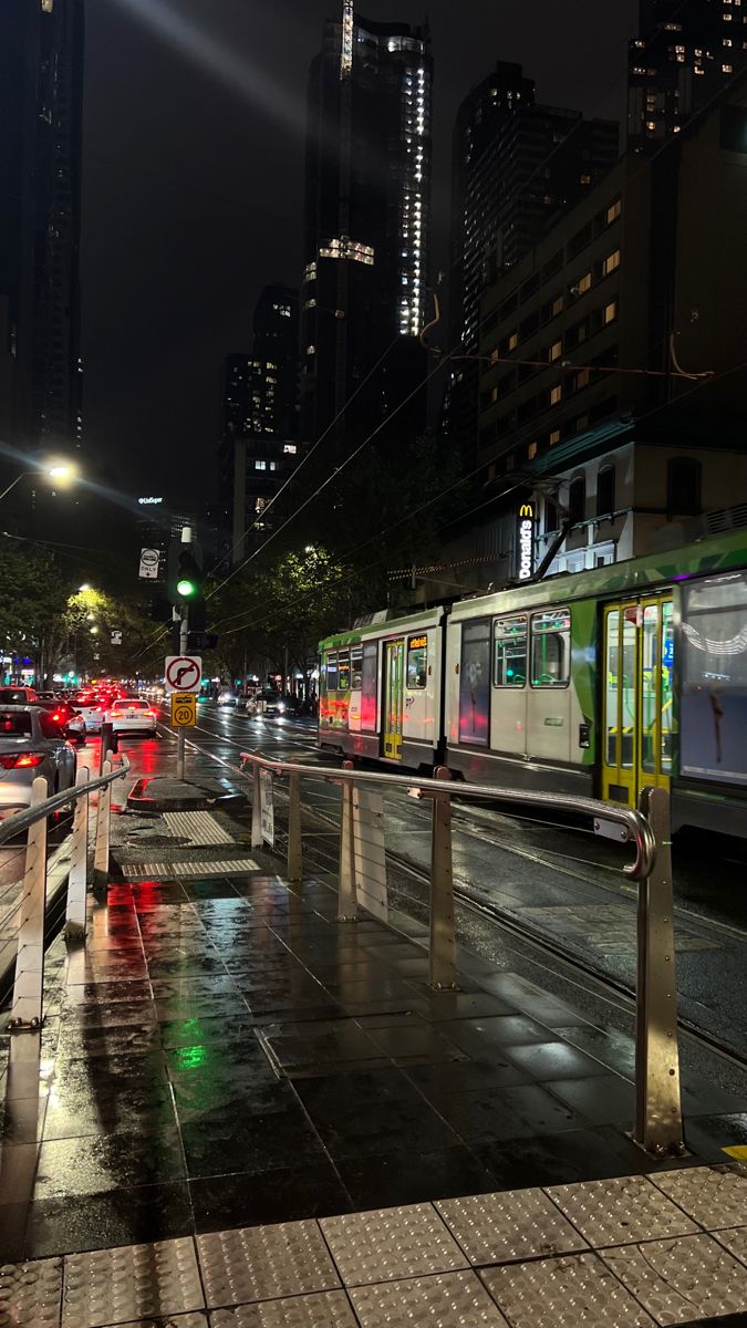 a city street filled with lots of traffic next to tall buildings at night and lit up by bright lights