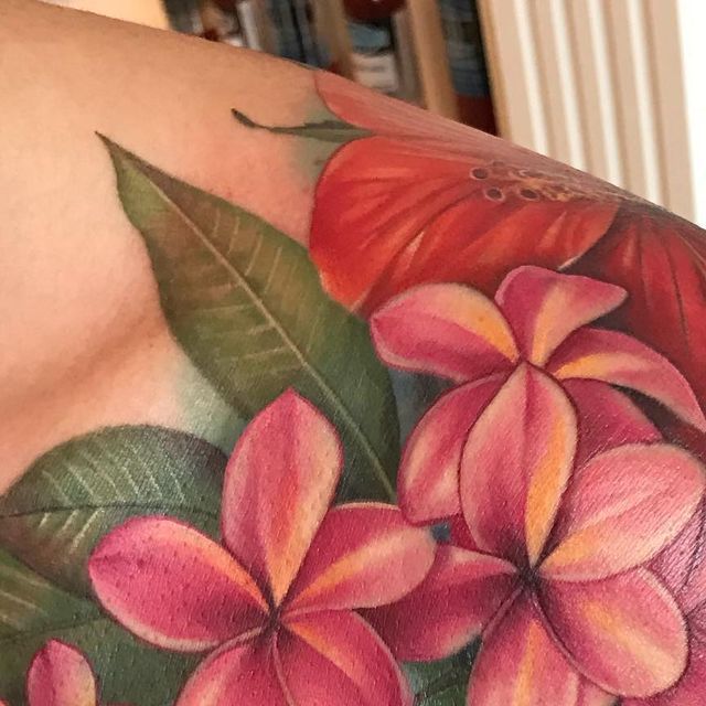 a close up of a person's back with flowers on it and green leaves