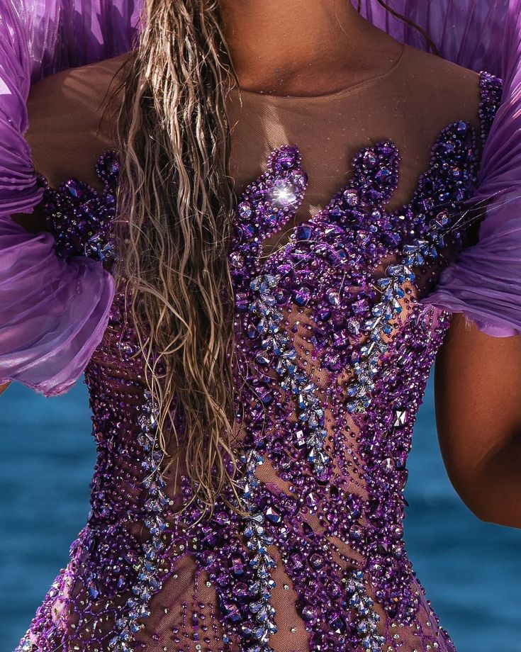 a woman in a purple dress with feathers on her head and hands behind her back