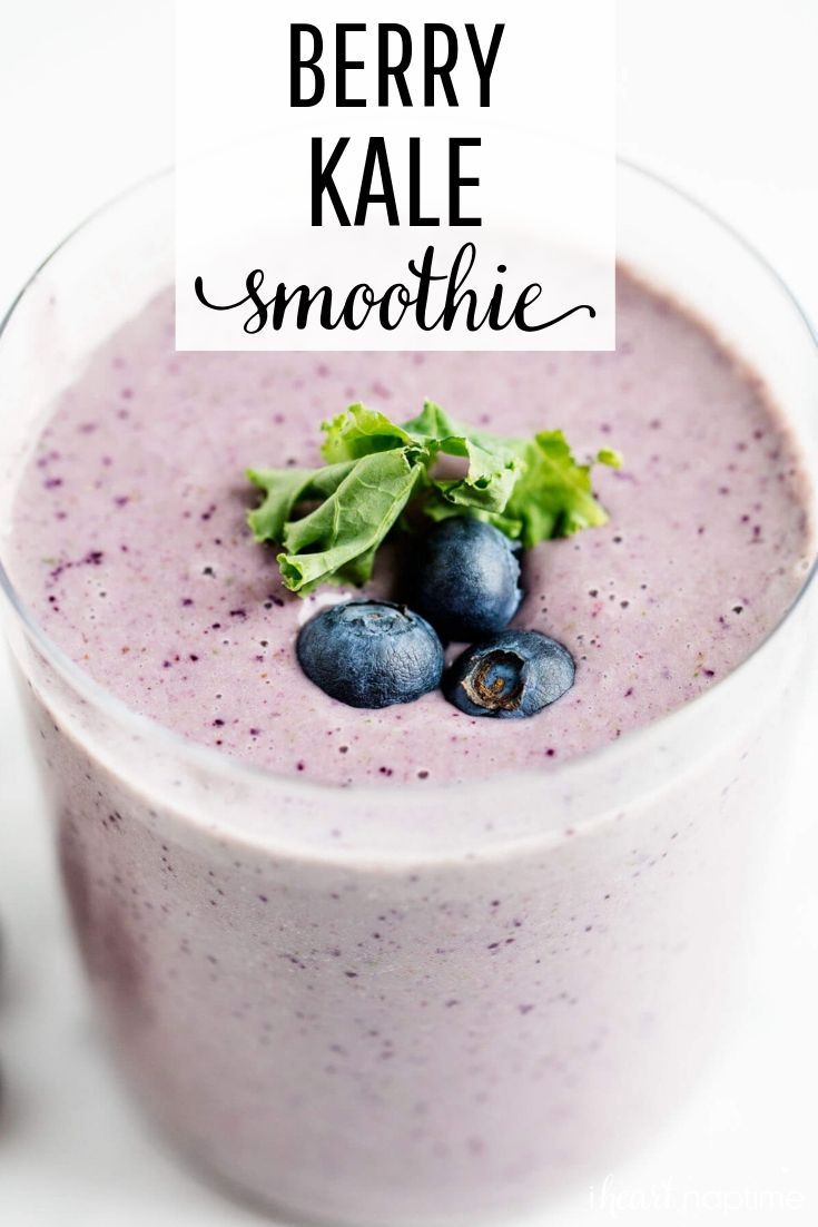 berry kale smoothie in a glass with blueberries on top and green leafy garnish