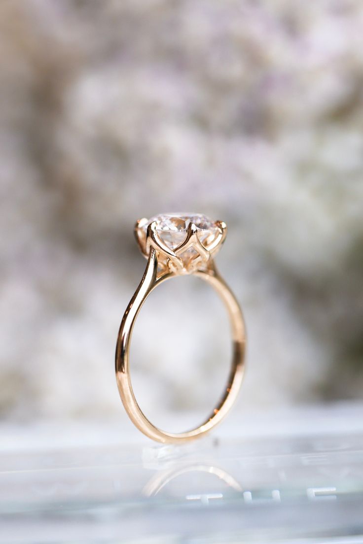 a gold ring with a white diamond on it sitting on a glass surface in front of a blurry background