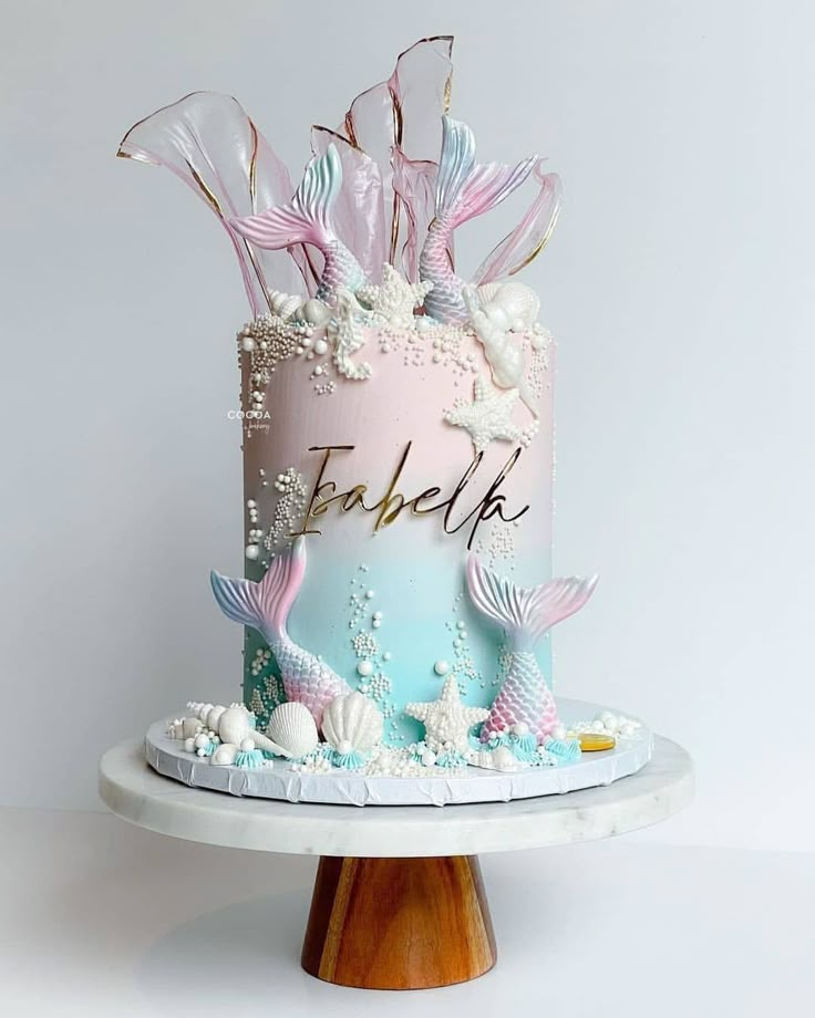 there is a pink and blue cake with mermaid decorations on the top that says fabelke