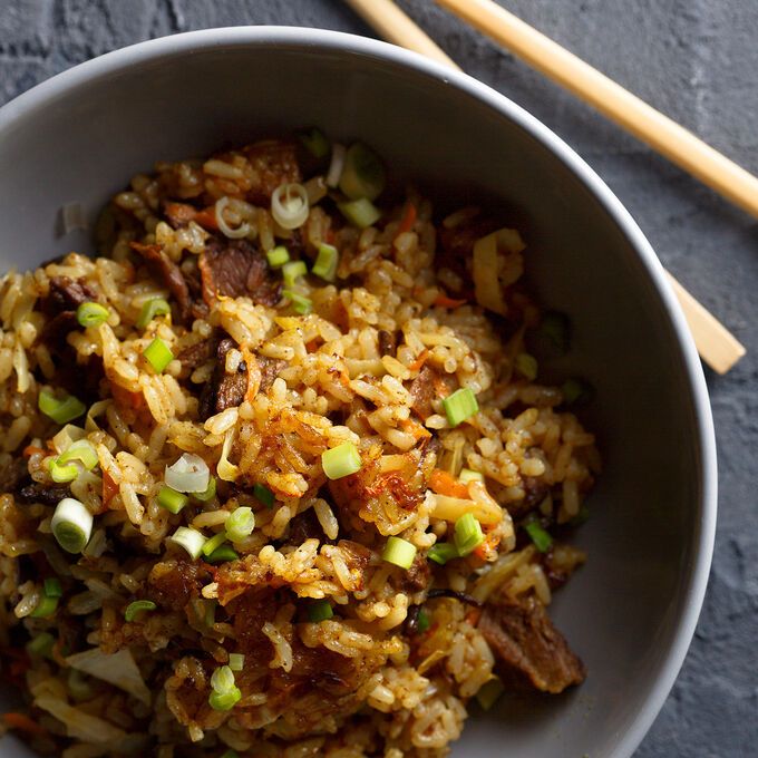 a white bowl filled with rice and meat next to chopsticks on a table