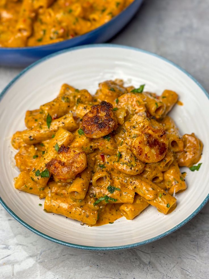 pasta with shrimp and tomato sauce in a white bowl next to a blue casserole dish