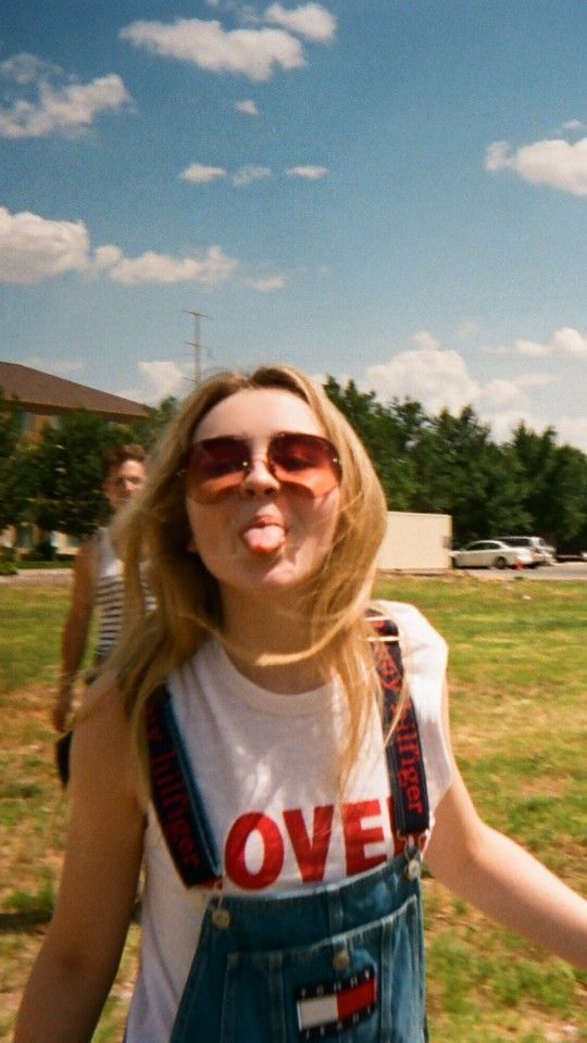 a woman in overalls and sunglasses making a funny face