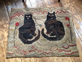 two black cats sitting on top of a rug