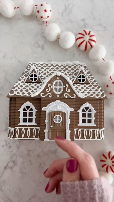 a hand holding up a gingerbread house cutout with candy canes around it