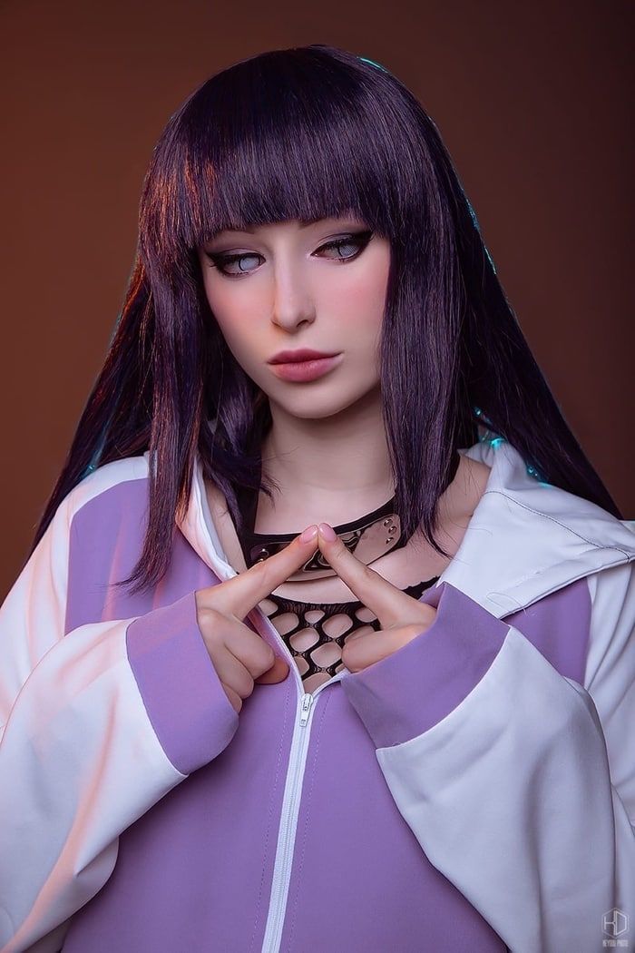 a woman with long black hair wearing a purple and white jacket holding her hands in the shape of a heart