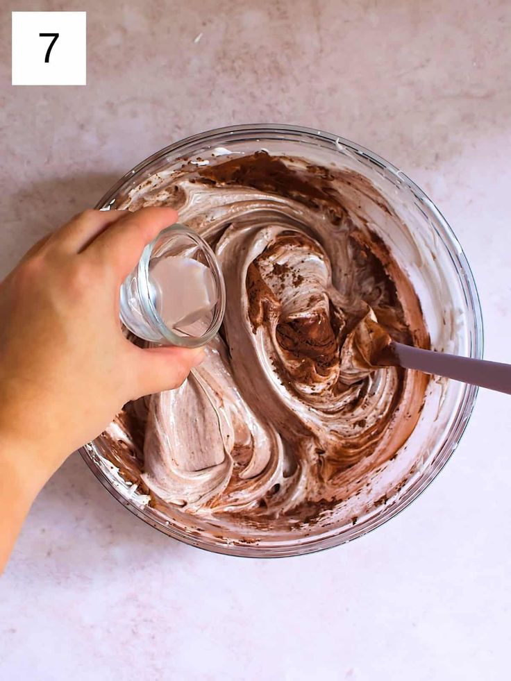 someone is spreading chocolate frosting on top of the cake in a glass bowl with a spatula