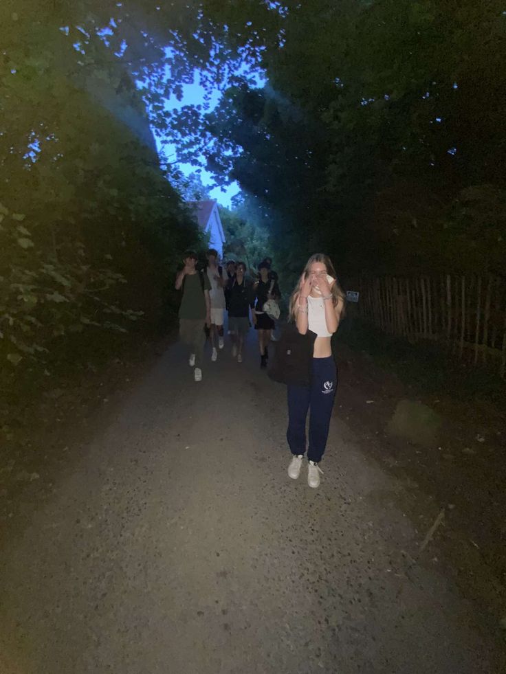 a group of people walking down a dirt road at night with their arms in the air