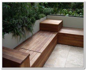 a wooden bench sitting on top of a tiled floor next to a lush green wall