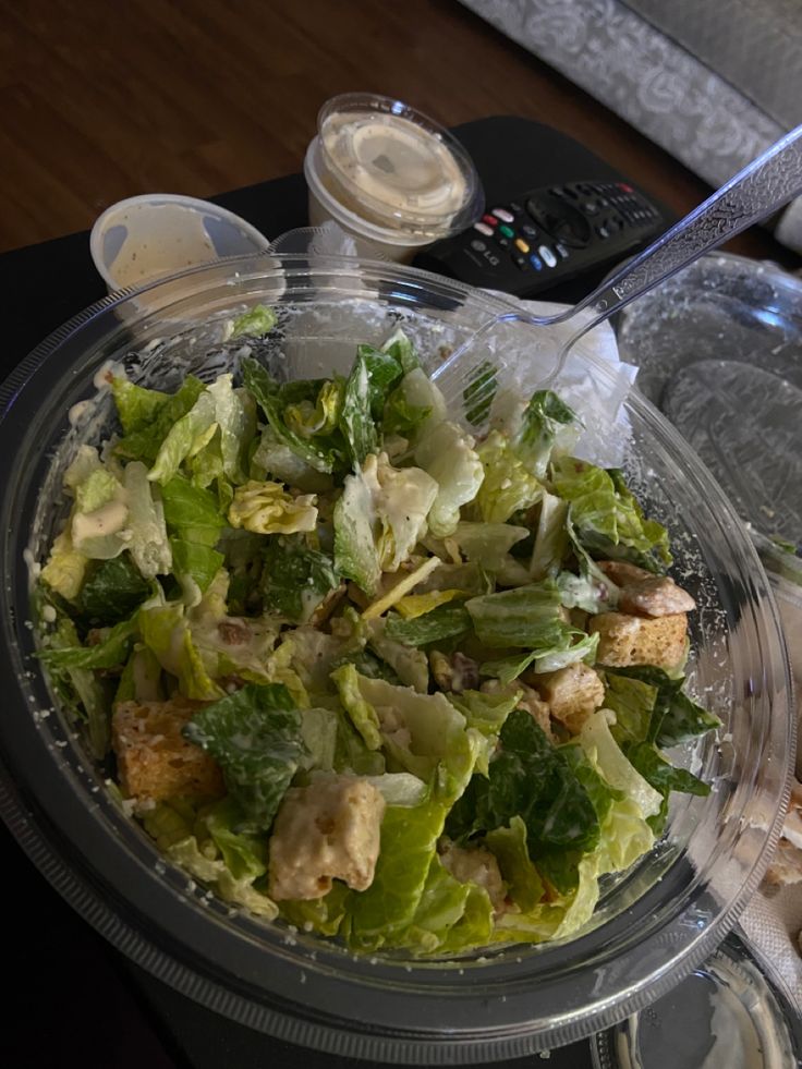 a salad in a plastic container on top of a table next to a remote control