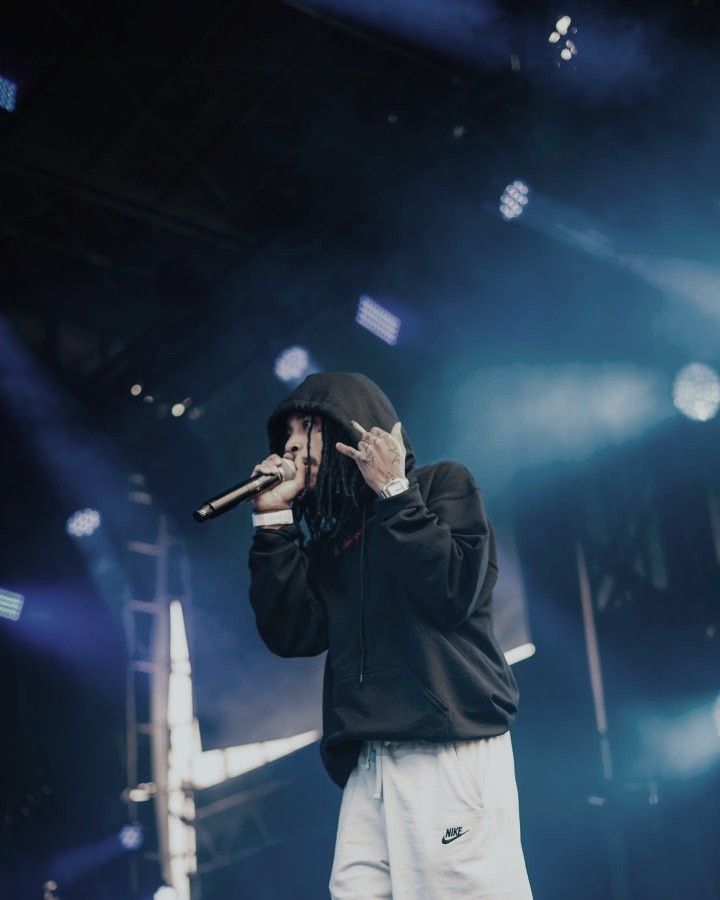 a man standing on top of a stage holding a microphone in his hand and wearing a black hoodie