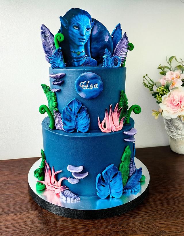 a three tiered cake with blue frosting and flowers on the top, sitting on a wooden table