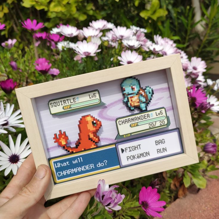 a person holding up a video game frame in front of some flowers and daisies