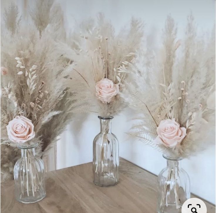 three glass vases with flowers in them sitting on a wooden table next to a mirror