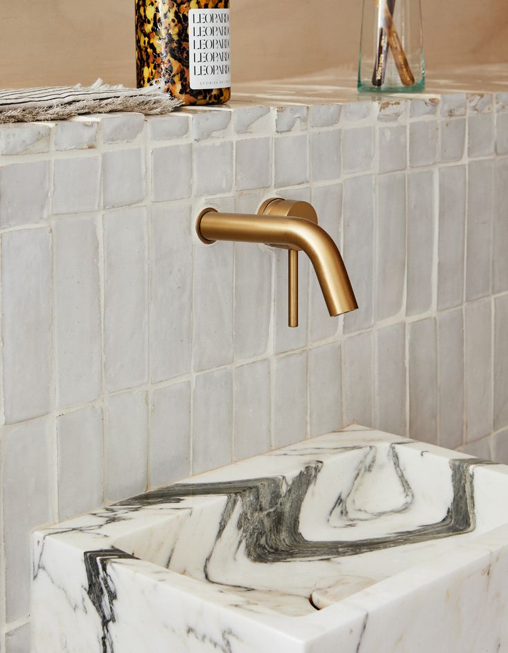 a marble sink with gold faucet and soap dispenser in the background