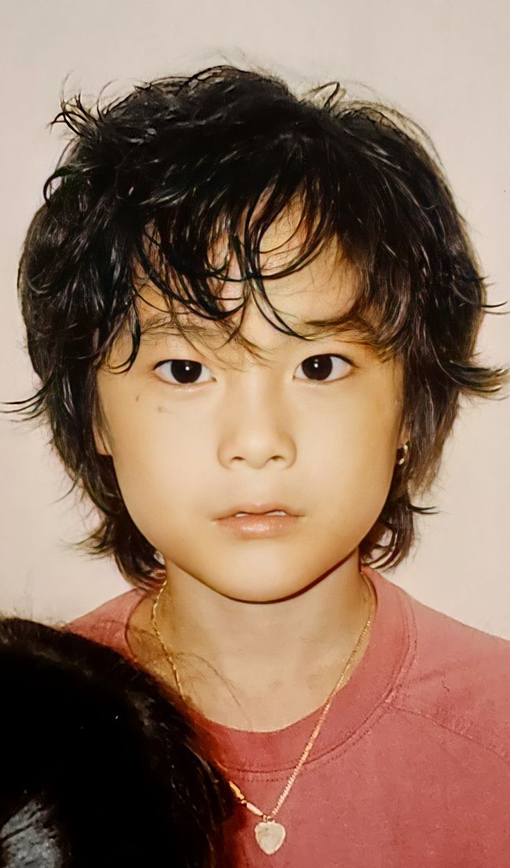 a young boy with black hair wearing a red shirt