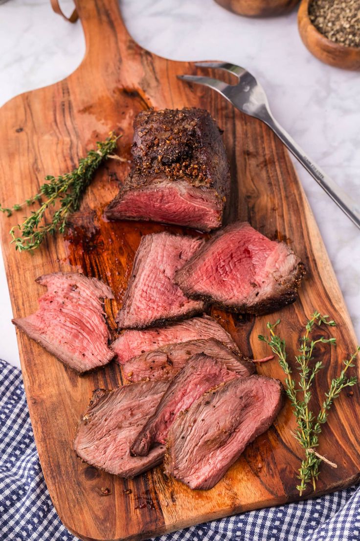 sliced beef on a cutting board with herbs and seasoning next to it, ready to be served