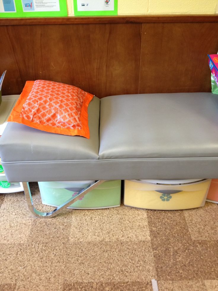 a gray leather bench with orange and green pillows on it in front of bookshelves