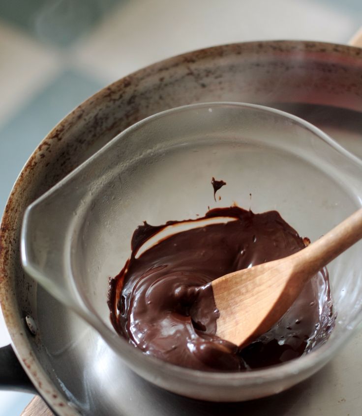 a wooden spoon sitting in a bowl filled with melted chocolate on top of a table