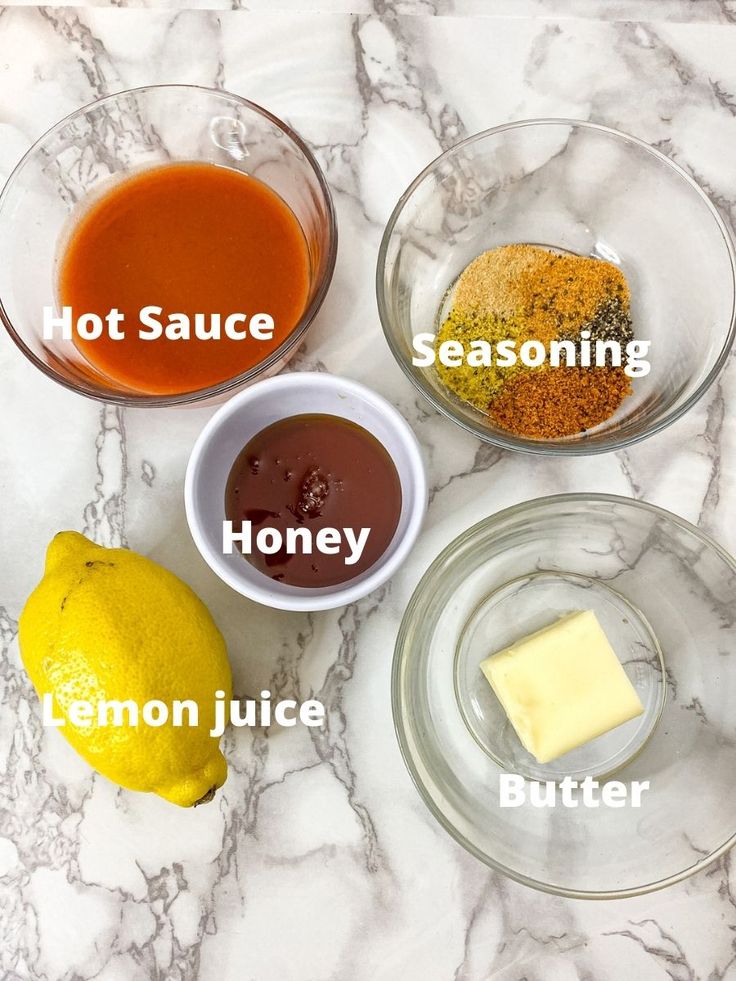 four bowls with different types of sauces in them on a marble counter top next to two lemons