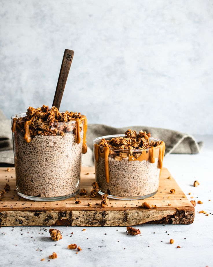 two glasses filled with oatmeal sitting on top of a cutting board