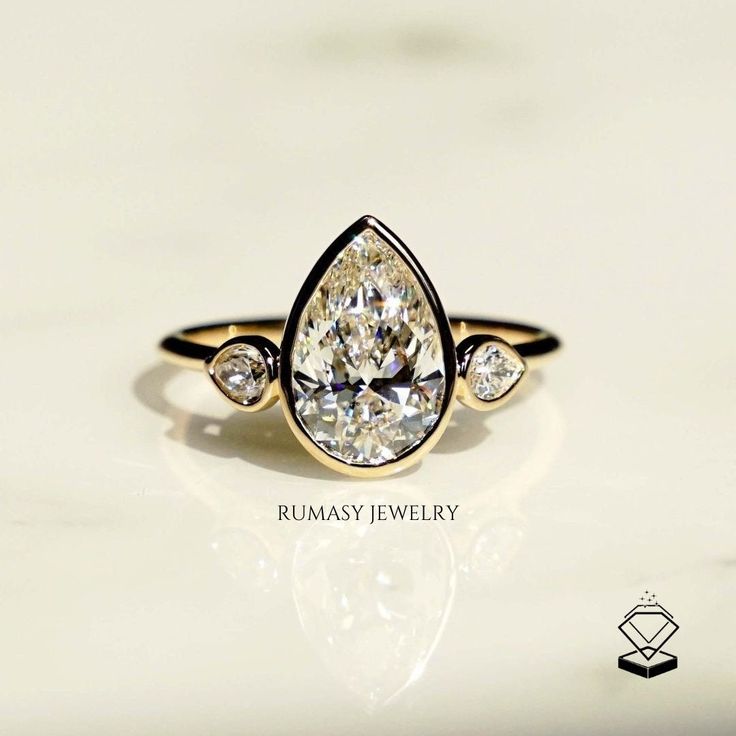 a yellow gold ring with three pear shaped diamonds on the side and an oval diamond in the middle