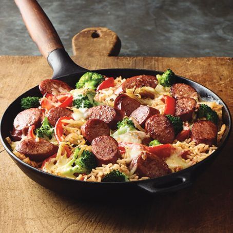 a skillet filled with sausage, broccoli and noodles on top of a wooden table