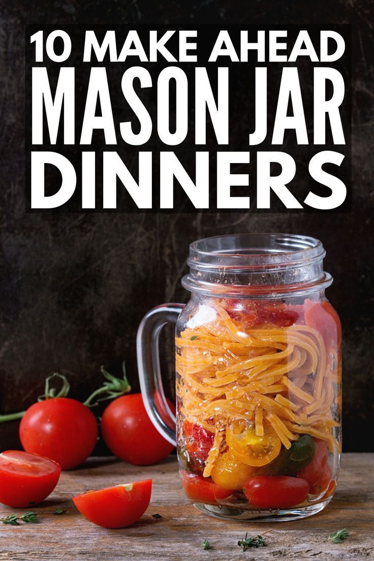 mason jar filled with pasta and tomatoes on top of a wooden table next to other vegetables