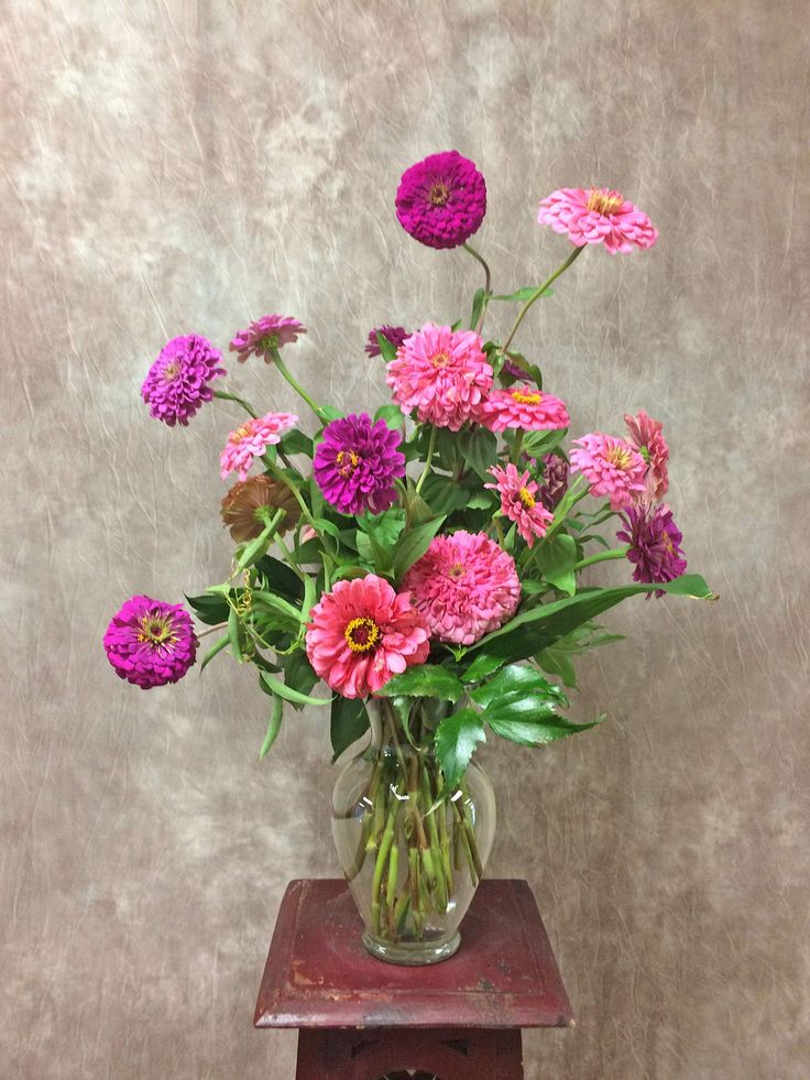 a vase filled with pink flowers sitting on top of a wooden table next to a wall