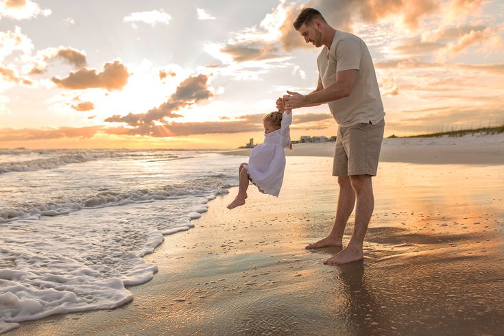 a father and daughter playing on the beach at sunset