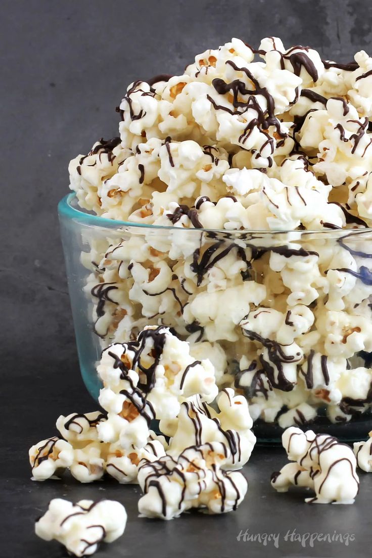 chocolate covered popcorn in a glass bowl on top of a black tablecloth with white and brown drizzled sprinkles