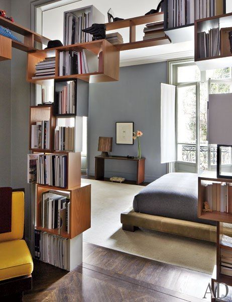 a book case with books on it in the middle of a room next to a bed