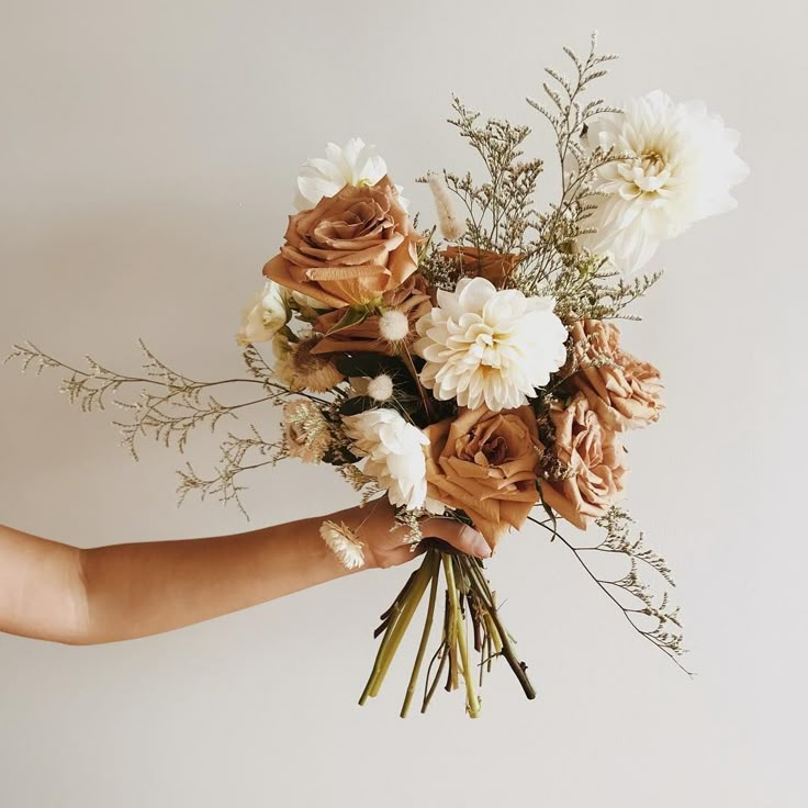 a person holding a bouquet of flowers in their hand with white and brown flowers on it