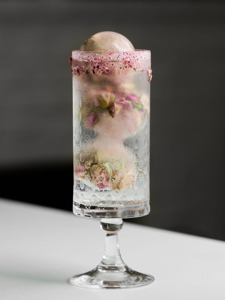 a glass filled with ice and flowers on top of a white countertop next to a black wall