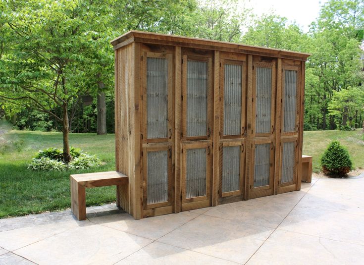 a wooden bench sitting in front of a large outdoor storage shed with glass doors on it's sides