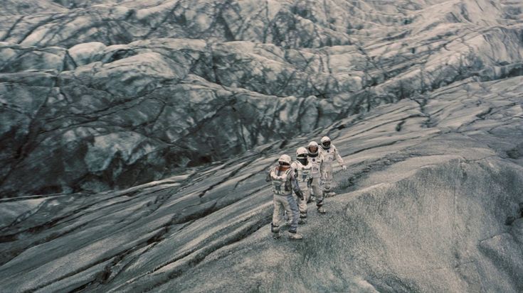 three astronauts are walking on the edge of a large rock formation with mountains in the background